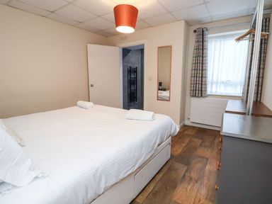 A bedroom with a double bed two rolled towels a dresser a window with curtains and a mirror on the wall at Cadwaladr in Bontnewydd near Caernarfon