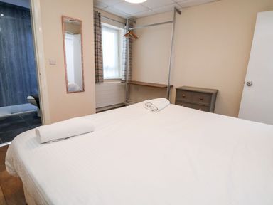A bedroom with a bed with towels a wall mirror a small dresser a window and an open door to a bathroom at Cadwaladr in Bontnewydd near Caernarfon