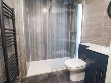A bathroom with a shower area a toilet a sink with dark cabinets and a towel radiator at Cadwaladr in Bontnewydd near Caernarfon