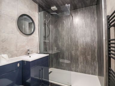 A bathroom with a sink and cabinet a round mirror and a glass enclosed shower area at Cadwaladr in Bontnewydd near Caernarfon