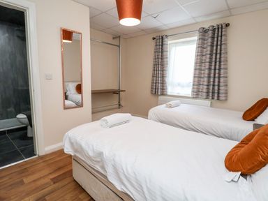 A bedroom with two single beds each with a rolled towel and orange pillows a wall mirror a window with patterned curtains and a doorway to a bathroom at Cadwaladr in Bontnewydd near Caernarfon