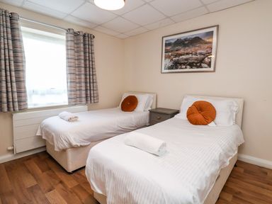 A bedroom with two single beds a nightstand window with curtains and a framed picture on the wall at Cadwaladr in Bontnewydd near Caernarfon