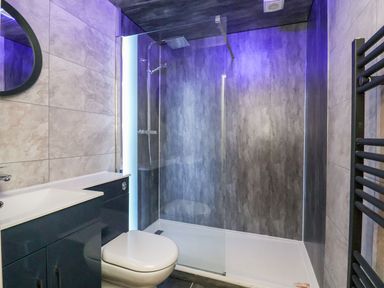 A bathroom with a shower area with glass screen a toilet a sink with cabinet and a heated towel rail at Cadwaladr in Bontnewydd near Caernarfon