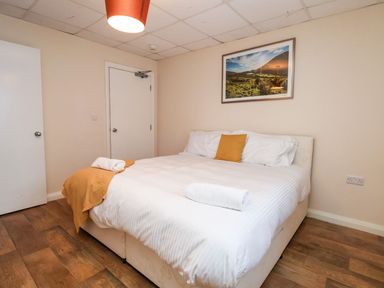 A bedroom with a double bed white bedding wooden floor and a landscape picture on the wall at Cadwaladr in Bontnewydd near Caernarfon