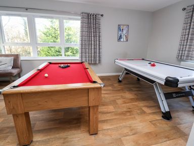 A game room with a red pool table and a white air hockey table at Cadwaladr in Bontnewydd near Caernarfon