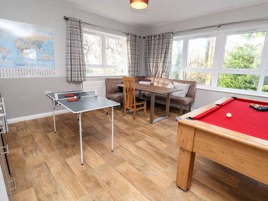A room with a ping pong table an L-shaped bench with pillows and a table and a pool table with a red cloth at Cadwaladr in Bontnewydd near Caernarfon