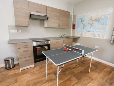 A kitchen with wooden cabinets a stove a sink a trash can and a ping pong table with paddles and a ball at Cadwaladr in Bontnewydd near Caernarfon