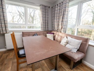 A dining area with a wooden chair a rectangular table and an L-shaped bench with cushions at Cadwaladr in Bontnewydd near Caernarfon