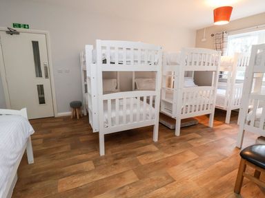 A bedroom with multiple white bunk beds wooden floor and a window with curtains at Cadwaladr in Bontnewydd near Caernarfon