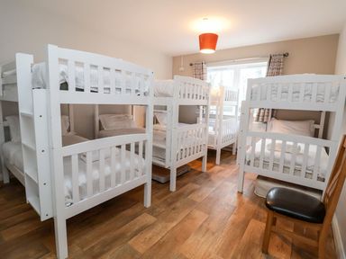 A bedroom with multiple white bunk beds and a wooden chair at Cadwaladr in Bontnewydd near Caernarfon