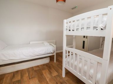 A bedroom with a single bed and a white bunk bed on wooden flooring at Cadwaladr in Bontnewydd near Caernarfon