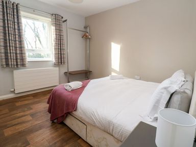 A bedroom with a bed with white linens and a folded towel on a blanket near a window with patterned curtains at Cadwaladr in Bontnewydd near Caernarfon
