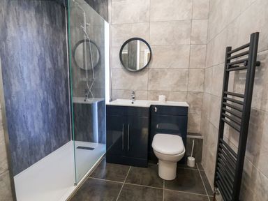 A bathroom with a walk in shower toilet sink cabinets round mirror and towel radiator at Cadwaladr in Bontnewydd near Caernarfon