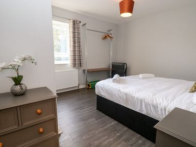 A bedroom with a bed, chest of drawers, open clothes rack with hangers, a window and a plant on the drawer at Cadwaladr in Bontnewydd near Caernarfon