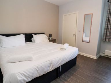A bedroom with a double bed two rolled towels a bedside table with a lamp a wall mirror and a door at Cadwaladr in Bontnewydd near Caernarfon