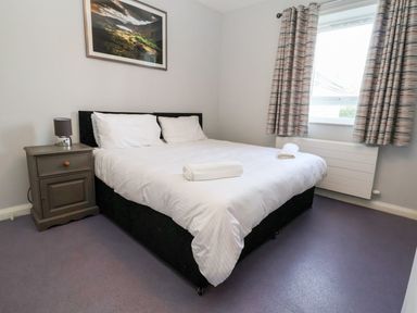 A bedroom with a double bed bedside table lamp window and curtains at Cadwaladr in Bontnewydd near Caernarfon