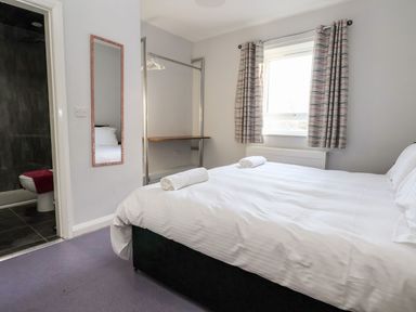 A bedroom with a bed with white linens two rolled towels a window with curtains a mirror open closet and a bathroom entrance at Cadwaladr in Bontnewydd near Caernarfon