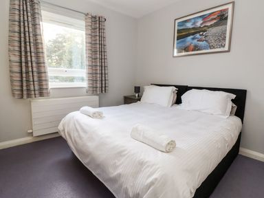 A bedroom with a double bed with white linens and rolled towels near a window with curtains at Cadwaladr in Bontnewydd near Caernarfon