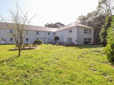 An outdoor grassy area with a leafless tree and tables with chairs near a two-story building at Cadwaladr in Bontnewydd near Caernarfon