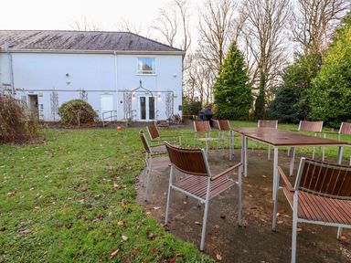 Outdoor seating area with wooden chairs and tables on a paved surface near a white building at Cadwaladr in Bontnewydd near Caernarfon
