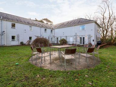 An outdoor seating area with metal and wood chairs around a table on a concrete circle in a grassy yard with a two-story building in the background at Cadwaladr in Bontnewydd near Caernarfon