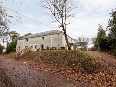 A two-story building with picnic tables outside on a grassy hill surrounded by trees at Cadwaladr in Bontnewydd near Caernarfon