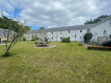 A courtyard with grass a tree a table with chairs and surrounding buildings at Cadwaladr in Bontnewydd near Caernarfon