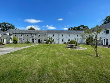 A courtyard with grass lawn tables chairs and trees surrounded by two-story buildings at Cadwaladr in Bontnewydd near Caernarfon