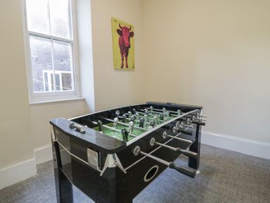 A foosball table in a small room with a window and a picture of a cow on the wall at The Lombard in Dolgellau