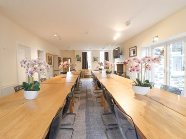 A dining room with long wooden tables and plastic chairs with flower pots on tables at The Lombard in Dolgellau