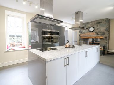 A kitchen with a large island and stovetops a stone fireplace with a clock and double ovens at The Lombard in Dolgellau