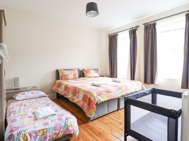 A bedroom with a double bed a single bed a baby crib wooden floor and windows with curtains at The Lombard in Dolgellau