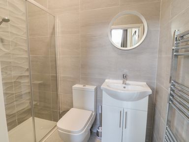 A bathroom with a shower enclosure toilet sink with cabinet round mirror and towel rack at The Lombard in Dolgellau