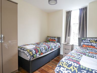 A bedroom with two single beds with colorful graffiti style bedding a bedside table with a lamp and a wardrobe at The Lombard in Dolgellau