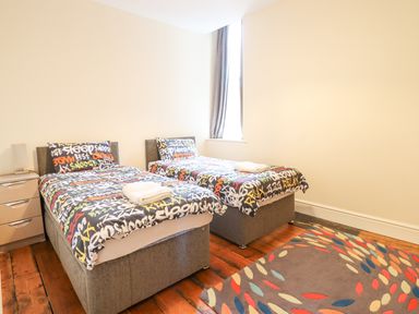 A bedroom with two single beds dressed with patterned bedding and a colorful rug on a wooden floor at The Lombard in Dolgellau