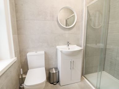 A bathroom with a toilet a sink with cabinet a round mirror and a glass shower enclosure at The Lombard in Dolgellau
