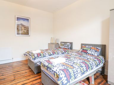 A bedroom with two single beds covered in printed bedspreads a dresser a radiator and a framed picture on the wall at The Lombard in Dolgellau