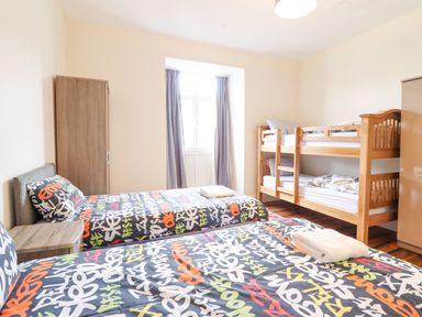 A bedroom with two single beds with colorful graffiti bedding a wooden bunk bed a wardrobe and a window with curtains at The Lombard in Dolgellau
