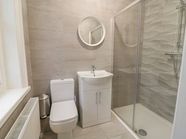 A bathroom with a toilet a sink with cabinet a round mirror a shower with glass door and textured tiles at The Lombard in Dolgellau