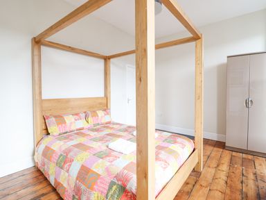 A bedroom with a wooden four-poster bed with a colorful patchwork duvet and pillows a beige wardrobe and wooden floorboards at The Lombard in Dolgellau
