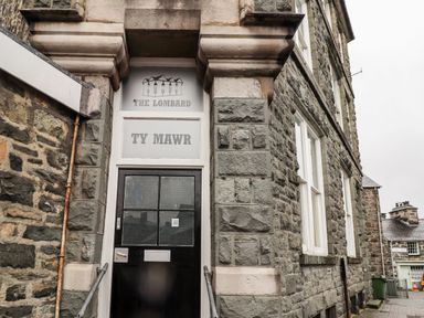 An entrance door with frosted glass panels and signs above that read The Lombard and TY MAWR on a stone building at The Lombard in Dolgellau