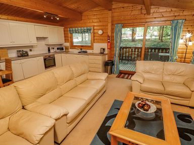A living room with beige sofas a wooden coffee table and a kitchen with white cabinets at Bamboo Retreat in Louth