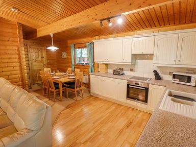 A kitchen and dining area with wooden walls and ceiling a dining table with six chairs a sofa and white kitchen cabinets at Bamboo Retreat in Louth