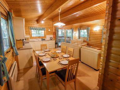 A wooden interior with a dining table set with plates and glasses next to a kitchen and a living area with cream sofas at Bamboo Retreat in Louth