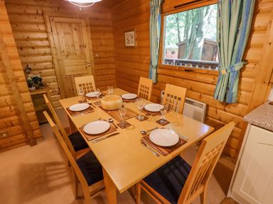 A dining area with a wooden table set for six with plates and glasses in a wooden cabin at Bamboo Retreat in Louth