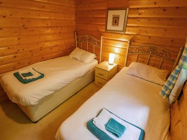 A bedroom with two single beds wooden walls and a nightstand with a lamp at Bamboo Retreat in Louth