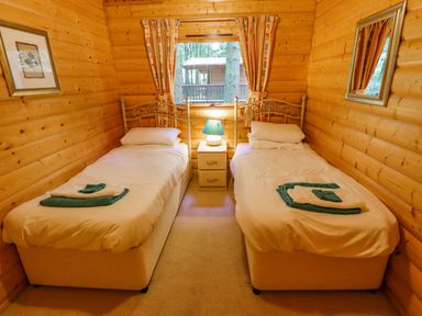 A bedroom with two single beds a nightstand with a lamp between them a window with curtains and wooden walls at Bamboo Retreat in Louth