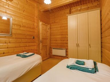 A bedroom with two single beds a wooden wardrobe a wall mirror and a wooden door at Bamboo Retreat in Louth