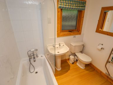A bathroom with a bathtub a sink a toilet a window with a blind and a wooden framed mirror at Bamboo Retreat in Louth