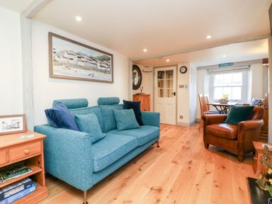 A living room with a blue sofa brown armchair wooden floor and dining table by the window at Peppers Cottage in Appledore